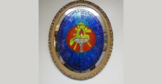 Photograph of an oval mirror painted in blue colors, with a silver flaming chalice in the middle.