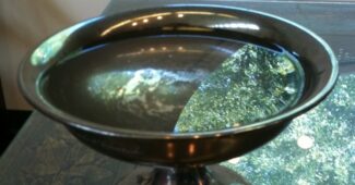 A large chalice with water reflecting a round window with trees outside.