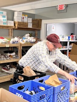 Man in dress shirt and ball cap loading several crates