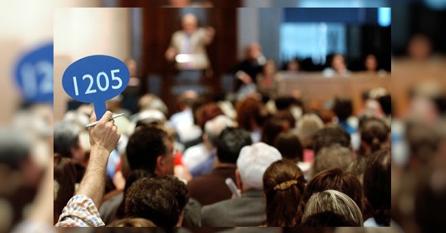Someone holds up auction paddle 1205 in a crowded room.
