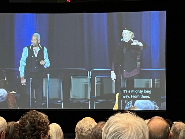 A Black man and a white man at microphones on a stage.