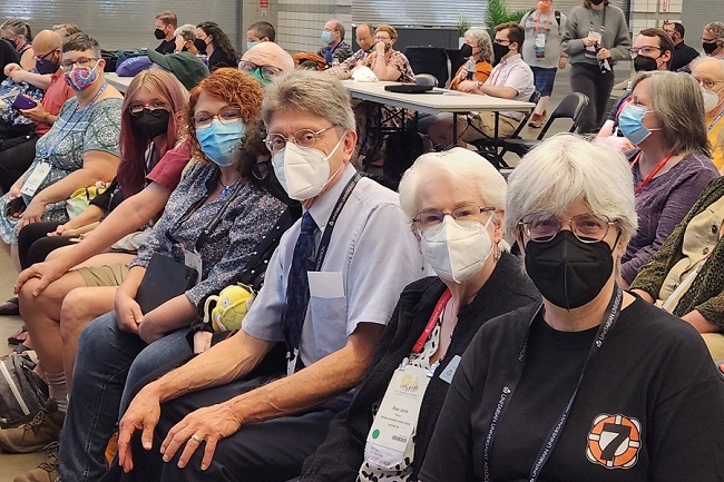 A line of people seated in the assembly hall look at the camera.