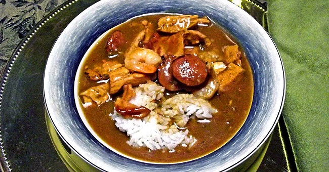 Bowl of gumbo with shrimp, sausage, and other ingredients in a dark broth.