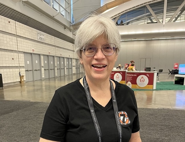 Woman smiling and looking at the camera, with an exhibit area in the background behind her.