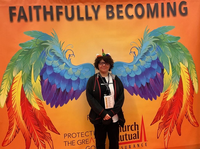 A teen stands in front of a huge banner that has painted angel wings.